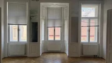 Großes Zimmer mit Fischgrätparkett, Erkerfenster und aufwendiger Stuckdecke, das viel Licht hereinlässt.