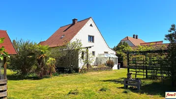 Hinteransicht des Hauses mit großem Garten, Gewächshaus und viel Grünfläche unter blauem Himmel.