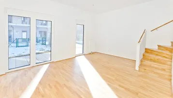 Helles Wohnzimmer mit Parkettboden, großen Fenstern und Zugang zu einem Außenbereich.