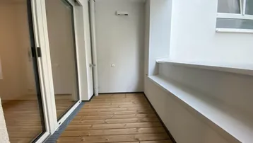 Heller Balkon mit Holzfußboden und großen Glasschiebetüren, ideal für entspannte Stunden im Freien.
