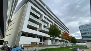 Moderne Wohnanlage mit weißer Fassade, Balkonen und begrüntem Innenhof unter bewölktem Himmel.
