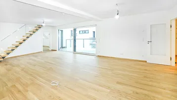 Geräumiger, heller Wohnbereich mit modernem Holzparkett, offener Treppe und Zugang zum Balkon.
