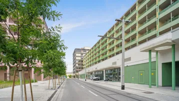 Moderne Wohngebäude entlang einer Straße mit Straßenbahnschienen und jungen Bäumen.