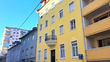 Gelbe Fassade eines Mehrfamilienhauses mit kleinem Balkon und Blick auf die Straße.