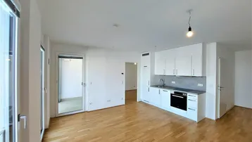 Heller, offener Wohnbereich mit integrierter Küchenzeile, Parkettboden und Zugang zum Balkon.