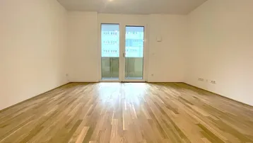Helles, leeres Zimmer mit Parkettboden und Zugang zu einem Balkon, ideal als Wohnbereich.