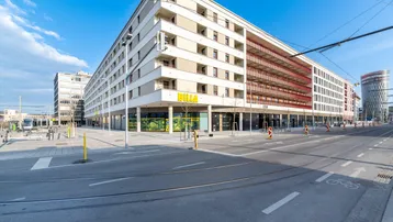 Modernes Wohngebäude mit Geschäften im Erdgeschoss und Straßenbahnhaltestelle in der Nähe.