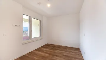 Ruhiges Schlafzimmer mit großen Fenstern und Blick ins Grüne, ausgestattet mit modernem Laminatboden.