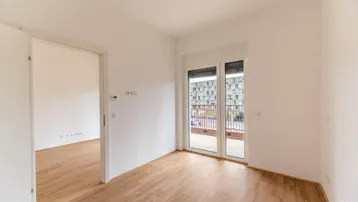 Helles Zimmer mit Parkettboden und Zugang zu einem Balkon, ideal für Wohn- oder Schlafbereich.