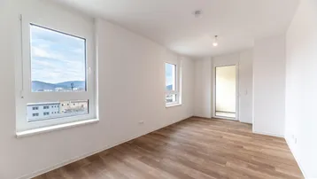 Helles, leeres Zimmer mit großen Fenstern und Holzboden, bereit zur individuellen Gestaltung.