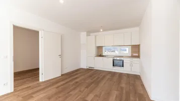 Funktionale, helle Küche mit weißen Schränken, integriertem Backofen und Laminatboden.