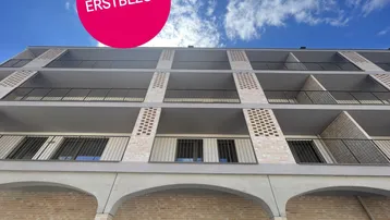 Moderne Wohnhausfassade mit Balkonen und einem Hinweis auf Erstbezug.