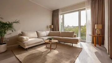 Helles Wohnzimmer mit großem Ecksofa, Teppich und Zugang zum Balkon mit Grünblick.