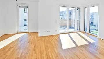 Heller Wohnbereich mit großen Fenstern, Holzboden und Zugang zu einer Terrasse.