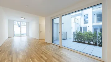 Helles, leeres Zimmer mit Parkettboden und Zugang zu einer Außenterrasse im Innenhof.