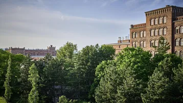 Historisches Backsteingebäude umgeben von üppigem Grün unter blauem Himmel.