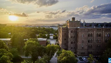 Historisches Gebäude mit Ziegelfassade und grüner Umgebung bei Sonnenuntergang, bietet weite Ausblicke.