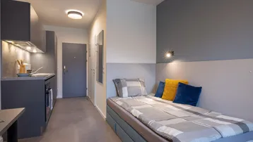 Modernes Studio-Apartment mit integrierter Küchenzeile und Schlafbereich in Grautönen.
