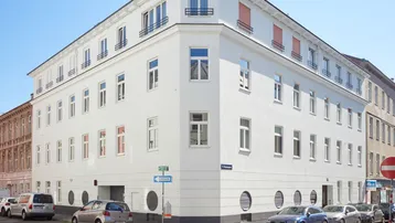 Modernes Eckgebäude mit weißer Fassade und vielen Fenstern an einer Stadtstraße.