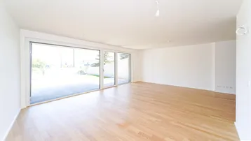 Helles, leeres Wohnzimmer mit großen Schiebetüren, die Zugang zu einer Terrasse bieten.