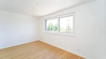 Helles Schlafzimmer mit Parkettboden und Blick ins Grüne durch das Fenster.