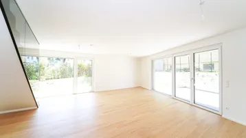Helles Wohnzimmer mit Parkettboden, großen Fenstern und Zugang zum Gartenbereich.
