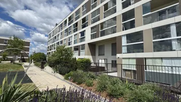 Moderne Wohnanlage mit großen Fenstern und gepflegter Grünfläche im Vordergrund unter bewölktem Himmel.
