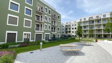 Moderner Innenhof mit grünen Rasenflächen, Sitzgelegenheiten und neuen Wohngebäuden in Pastellfarben.