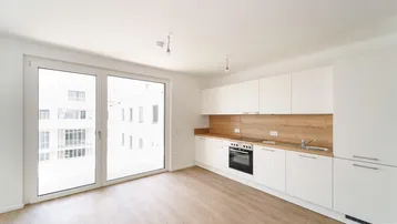 Helle, offene Küche mit modernen weißen Schränken, Holzarbeitsplatte und Zugang zum Balkon.