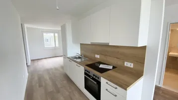 Moderne Einbauküche mit weißen Schränken, Holzoptik-Arbeitsplatte und integrierten Geräten in einem hellen Raum.