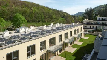 Moderne Wohnanlage mit Photovoltaikanlagen auf den Dächern und umgeben von grünen Hügeln.