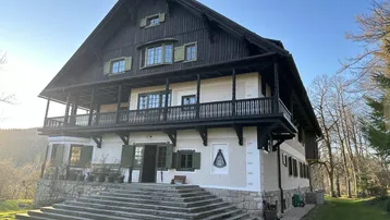 Großes, traditionelles Haus mit Holzfassade und mehreren Balkonen in ländlicher Umgebung.