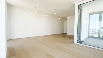 Heller, unmöblierter Wohnbereich mit Holzboden und großen Fenstern, die viel Tageslicht hereinlassen.