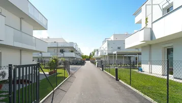 Blick auf eine moderne Wohnanlage mit weißen Gebäuden, gepflegten Rasenflächen und einem zentralen Weg.