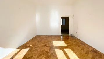 Geräumiges Zimmer mit Fischgrätparkett und Zugang zu weiteren Räumen.