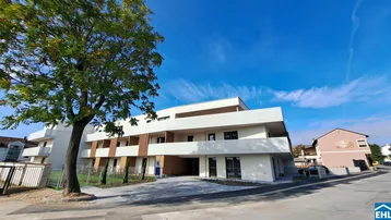 Neubau-Wohngebäude mit klarer Architektur, umgeben von Grünflächen und Bäumen.