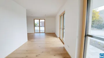 Heller, leerer Wohnraum mit großen Fenstern und Holzboden, der viel Tageslicht hereinlässt.