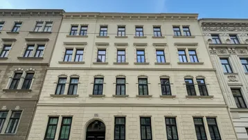 Klassische Fassade eines Altbaus mit vielen Fenstern und dekorativen Elementen unter blauem Himmel.