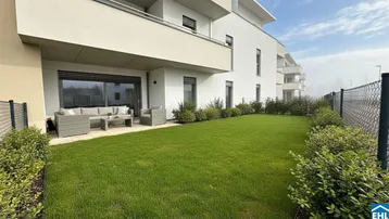 Große Terrasse mit modernen Gartenmöbeln und angrenzendem Rasenbereich vor einem Neubau.