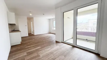 Heller Wohnbereich mit Holzboden, integrierter Küchenzeile und Zugang zu einem Balkon.