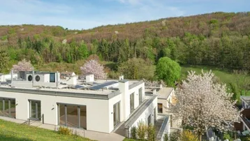 Moderne Gebäude in einer grünen Umgebung mit blühenden Bäumen und weitem Blick auf die Landschaft.