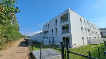 Moderne, weiße Neubauwohnungen mit Balkonen unter blauem Himmel, umgeben von Grünflächen und einem Weg.