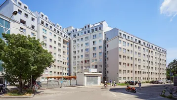 Großes Wohngebäude mit mehreren Etagen und Mansarddächern unter blauem Himmel.