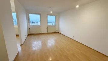 Helles, leeres Zimmer mit Laminatboden und zwei Fenstern, ideal als Wohn- oder Schlafbereich.