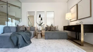 Stilvolles Wohnzimmer mit modernen Möbeln, großem Teppich und dekorativen Spiegeln an der Wand.