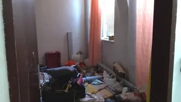 Ein unaufgeräumter Innenraum in einem renovierungsbedürftigen Zustand mit einem Fenster und Holzdecke.