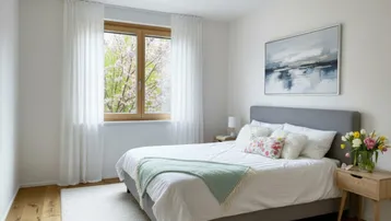 Helles Schlafzimmer mit Holzboden, großem Fenster und Blick ins Grüne mit blühenden Bäumen.