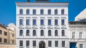 Weißes Altbaugebäude mit klassischer Fassade und vielen Fenstern an einer Stadtstraße.