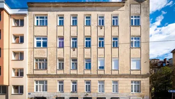 Fassade eines Altbaus mit vielen Fenstern und sichtbaren Gebrauchsspuren unter blauem Himmel.