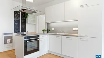 Moderne weiße Küche mit Kochinsel, integriertem Backofen und Dunstabzugshaube.